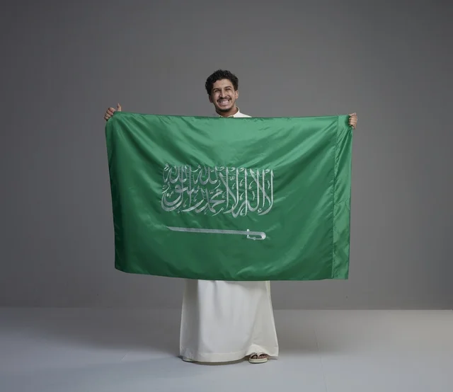 Smiling Saudi Man Holding National Flag in Studio Setting