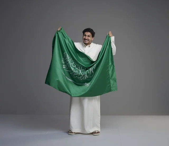 Saudi Man Holding National Flag in Traditional Thobe