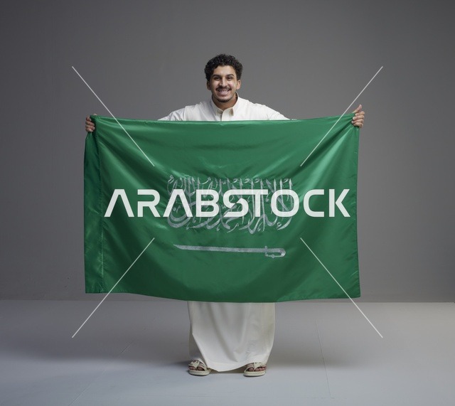 رجل سعودي يحمل علم السعودية على خلفية رمادية