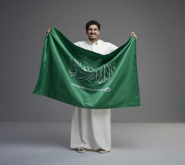 رجل سعودي يحمل العلم السعودي في استوديو بخلفية رمادية