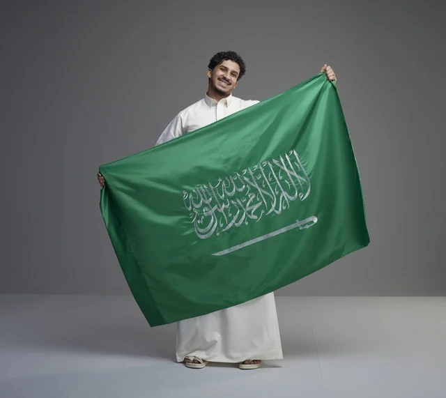 رجل سعودي يحمل علم المملكة في استوديو بخلفية رمادية