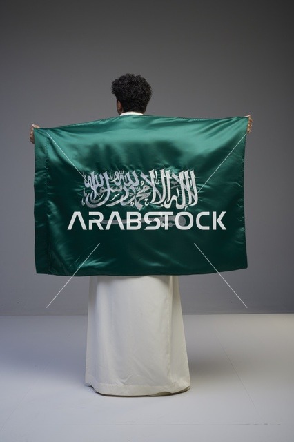 رجل سعودي يحمل علم المملكة العربية السعودية من الخلف
