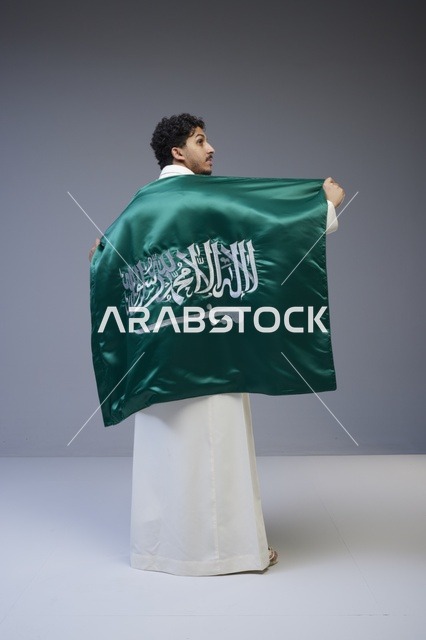 رجل سعودي يرتدي الثوب التقليدي ويحمل العلم الوطني السعودي