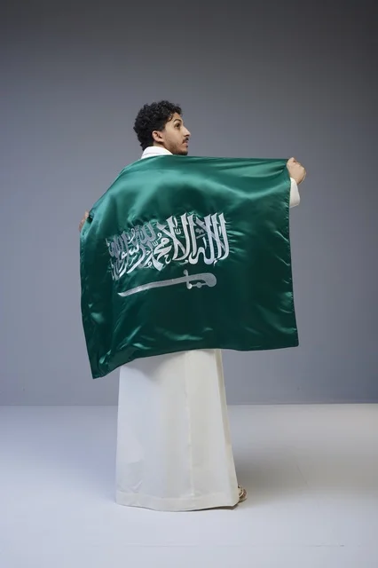 رجل سعودي يرتدي الثوب التقليدي ويحمل العلم الوطني السعودي
