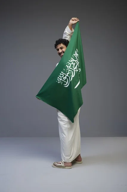 رجل سعودي يحمل العلم الوطني في استوديو رمادي