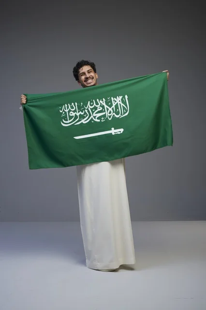 رجل سعودي يرتدي الثوب التقليدي يحمل العلم الوطني السعودي
