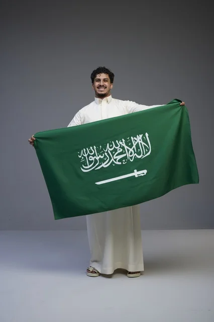 رجل سعودي يرتدي الثوب يحمل علم المملكة العربية السعودية