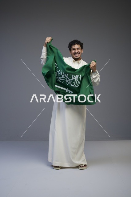 رجل سعودي يحمل العلم السعودي في استوديو تصوير