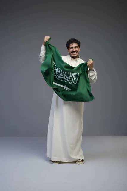 رجل سعودي يحمل العلم السعودي في استوديو تصوير
