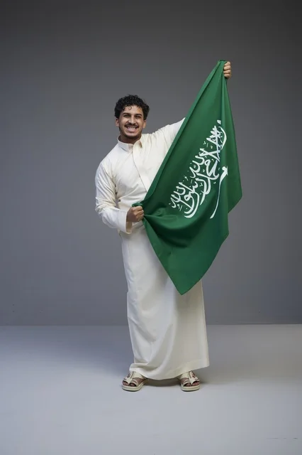 رجل سعودي يحمل العلم السعودي في استوديو بخلفية رمادية