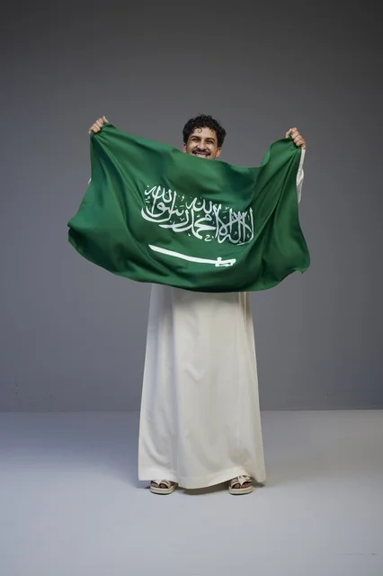 رجل سعودي يحمل العلم السعودي في استوديو تصوير