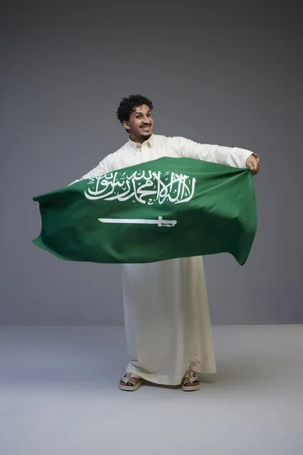 رجل سعودي يحمل العلم الوطني السعودي بالثوب التقليدي
