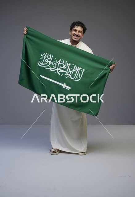 رجل سعودي بالثوب التقليدي يحمل علم المملكة العربية السعودية