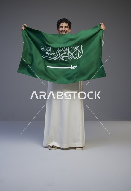 رجل سعودي بالثوب التقليدي يحمل علم المملكة العربية السعودية