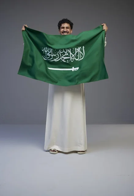 رجل سعودي بالثوب التقليدي يحمل علم المملكة العربية السعودية