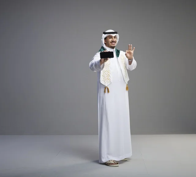خريج سعودي يحمل شاشة هاتف ذكي في استوديو