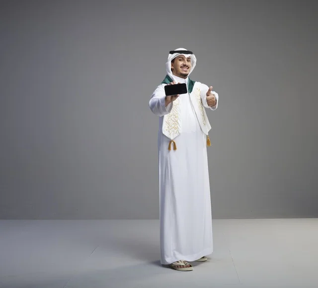 خريج سعودي يحمل هاتف ذكي مع إشارة الإعجاب