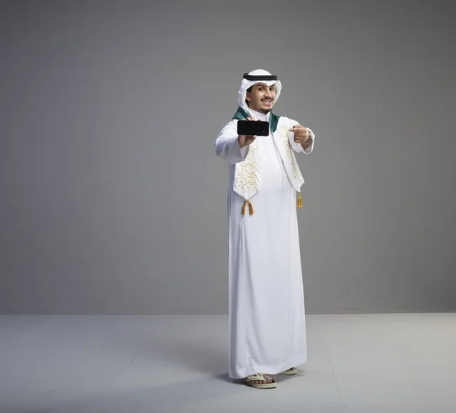 Saudi Graduate Holding Smartphone on Gray Background