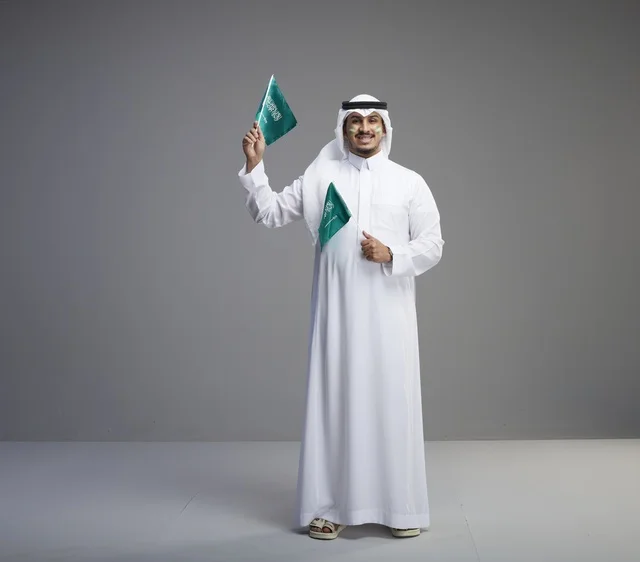 رجل سعودي يحمل الأعلام الوطنية بخلفية رمادية رجل سعودي يحمل الأعلام الوطنية بخلفية رمادية
