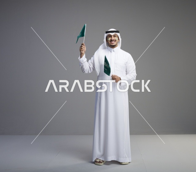رجل سعودي مبتسم يحمل علمين وطنيين