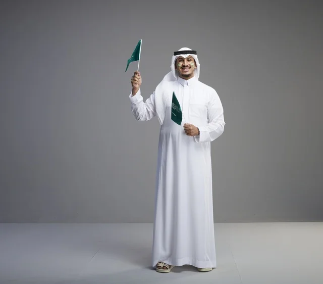 رجل سعودي مبتسم يحمل علمين وطنيين