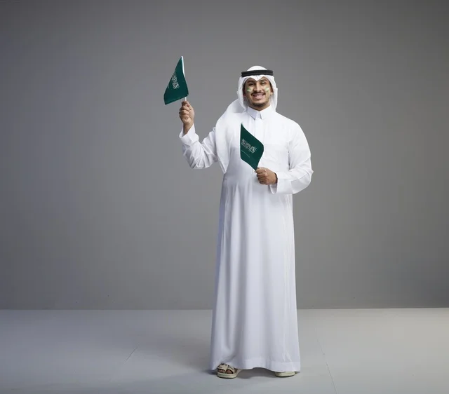 رجل سعودي مبتسم يحمل أعلام المملكة في الاحتفال