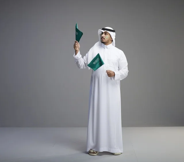 رجل سعودي يحمل الأعلام الوطنية في خلفية استوديو