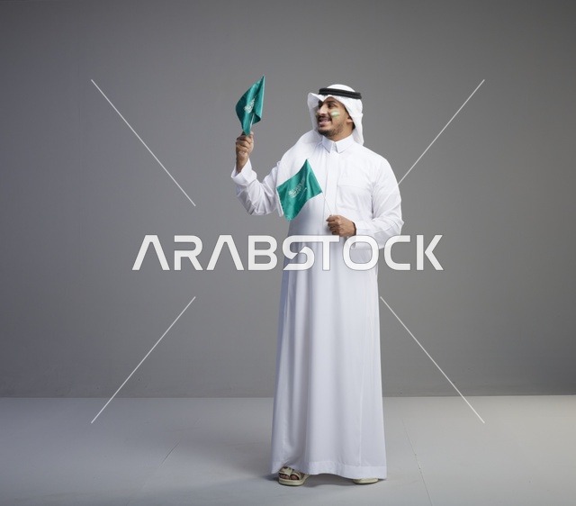 رجل سعودي مبتسم يحمل علمين وطنيين