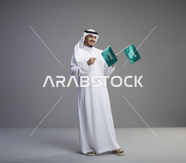 رجل سعودي مبتسم يحمل علمين وطنيين