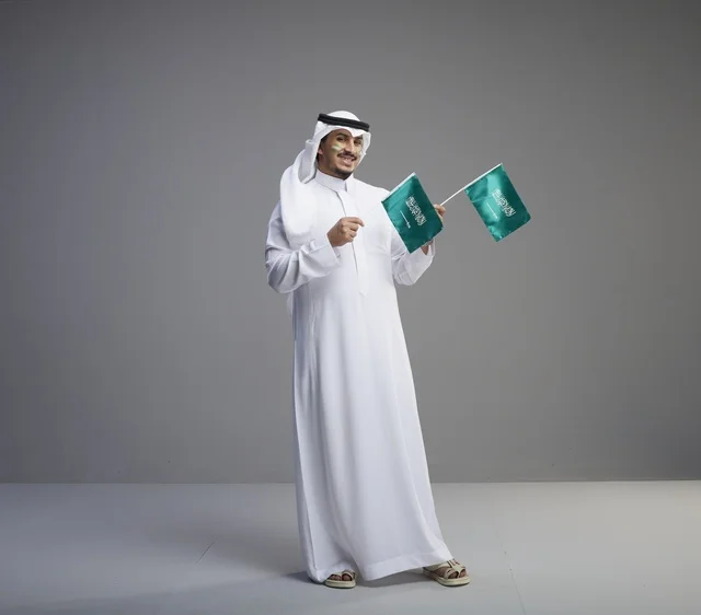 رجل سعودي مبتسم يحمل علمين وطنيين