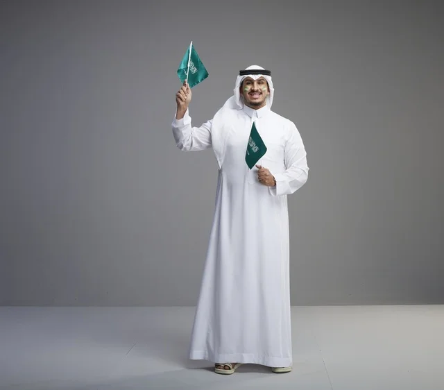 رجل سعودي مبتسم يحمل أعلام المملكة العربية السعودية