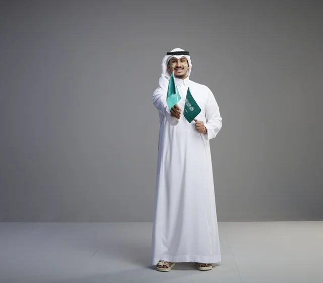 رجل سعودي بالثوب التقليدي يحمل العلم السعودي