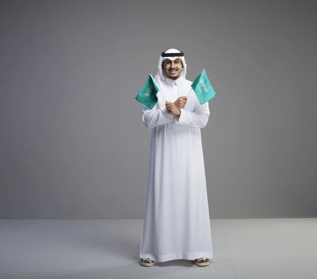 رجل سعودي بالزي التقليدي يحمل أعلام المملكة