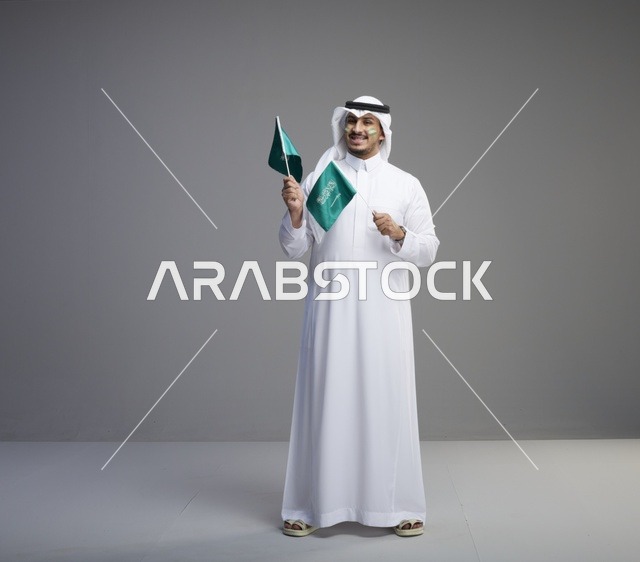 رجل سعودي يبتسم ويحمل أعلام المملكة العربية السعودية