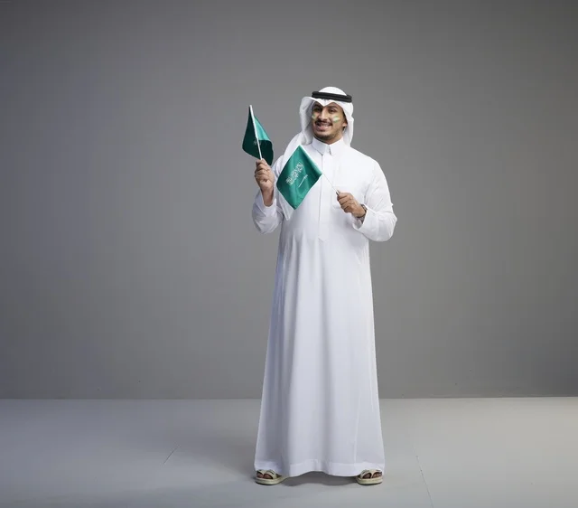 Smiling Saudi Man Holding KSA National Flags in Studio