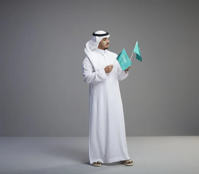 رجل سعودي بالثوب التقليدي يحمل أعلام المملكة العربية السعودية