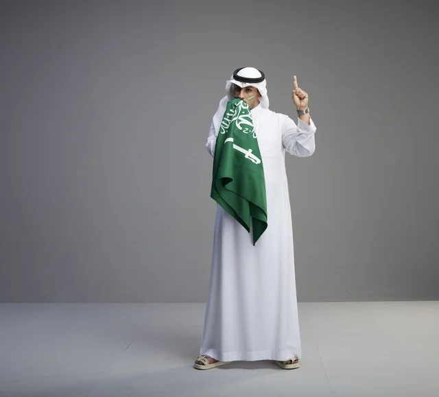 رجل سعودي بالزي التقليدي يقبل العلم السعودي
