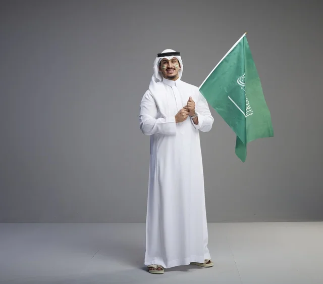 رجل سعودي يحمل العلم الوطني بخلفية رمادية