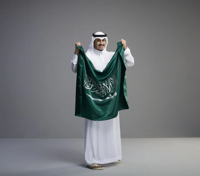رجل سعودي يحمل العلم الوطني بالزي التقليدي