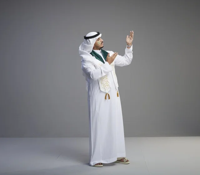 خريج سعودي بالزي التقليدي ووشاح التخرج يدعو في الاستوديو