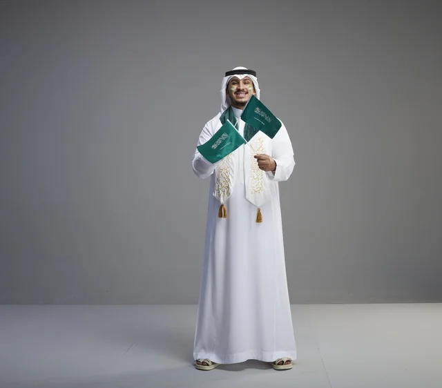 رجل سعودي يحمل الأعلام الوطنية بالزي التقليدي