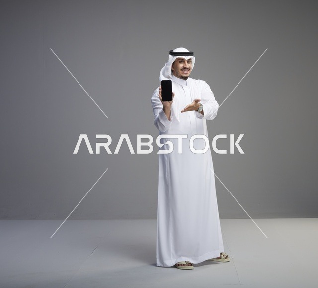 رجل سعودي يحمل هاتف بشاشة فارغة في الاستوديو