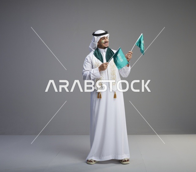 رجل سعودي يحتفل باليوم الوطني حاملاً الأعلام السعودية