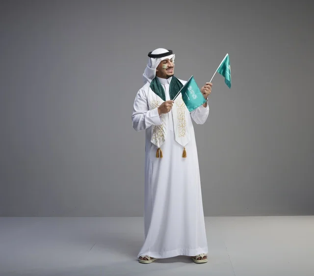 رجل سعودي يحتفل باليوم الوطني حاملاً الأعلام السعودية