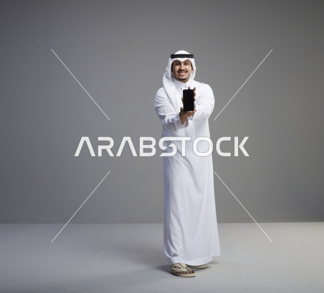 رجل سعودي يمسك بشاشة هاتف فارغة في الاستوديو