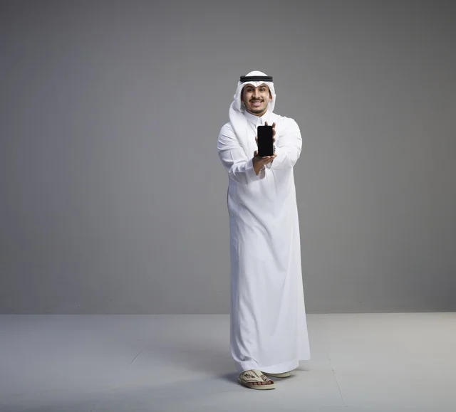 رجل سعودي يمسك بشاشة هاتف فارغة في الاستوديو