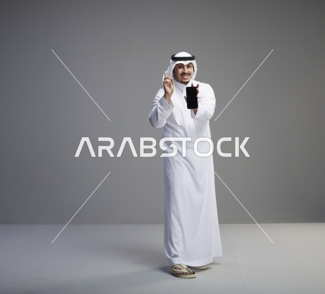 رجل سعودي يحمل هاتف ذكي بشاشة فارغة بخلفية رمادية