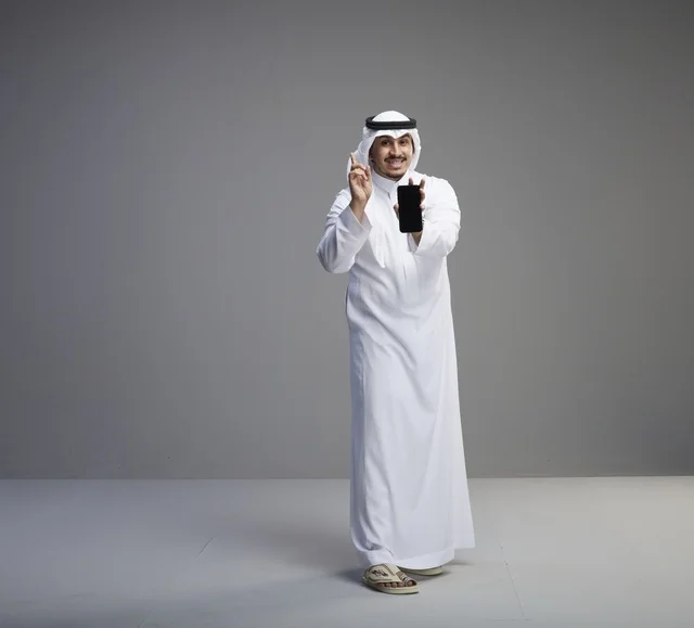 رجل سعودي يحمل هاتف ذكي بشاشة فارغة بخلفية رمادية