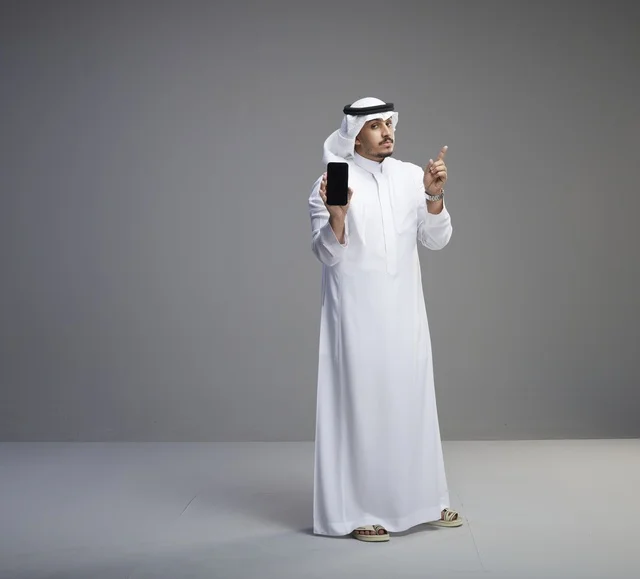 رجل سعودي يحمل هاتفاً ذكياً بشاشة فارغة بالثوب التقليدي