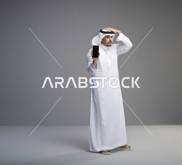 رجل سعودي يرتدي الثوب التقليدي يحمل هاتف ذكي بشاشة فارغة
